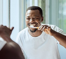 Man smiling while brushing his teeth in bathroom