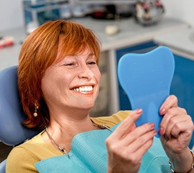 Woman in patient’s chair looking at her new dental implant in the mirror
