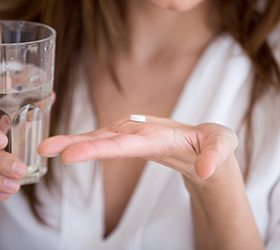 Woman in white robe holding pill and glass of water