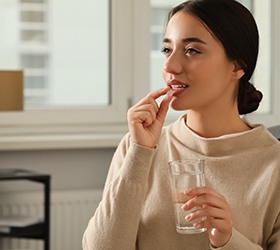 Woman in light brown sweater taking a pill