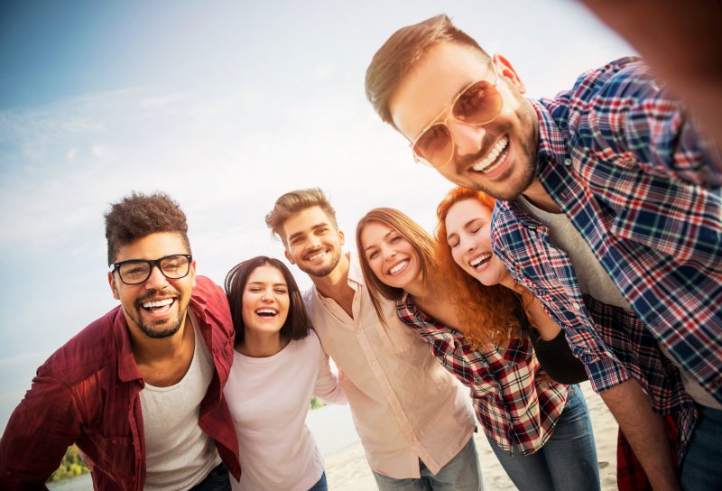 Patient smiling with their Invisalign on the beach with friends